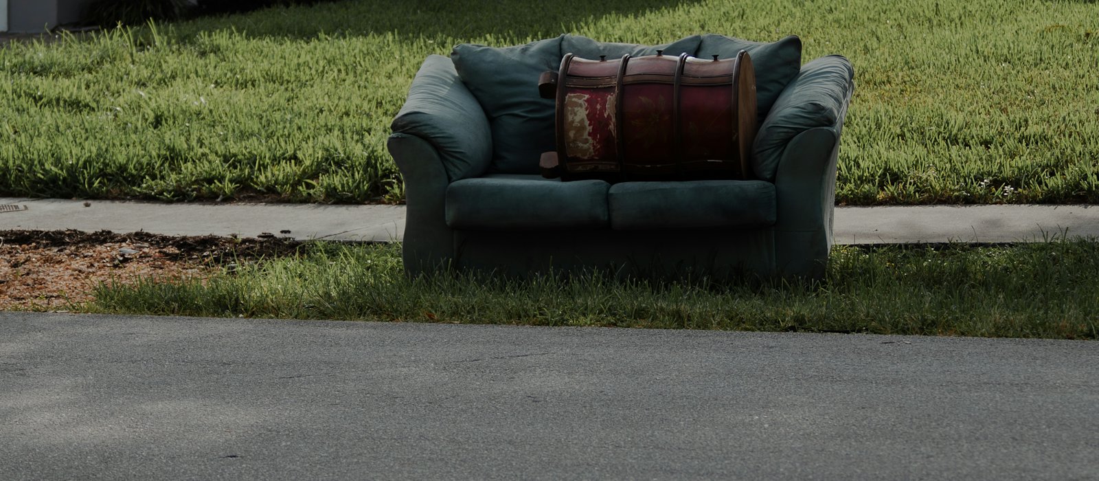 Old green couch left on a lawn at the curb, waiting to be hauled away