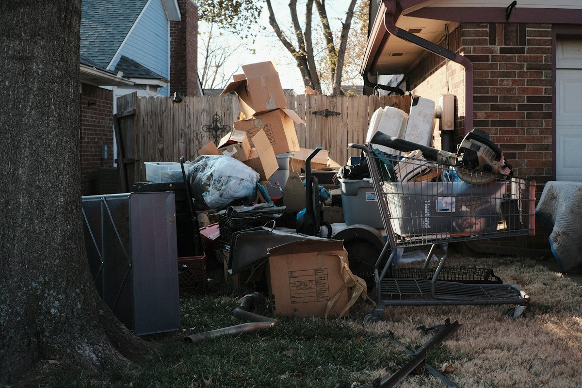 Pile of cardboard boxes, an old shopping cart and household junk beside a brick house